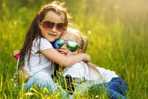 Two little girls standing together in the park, one hugs another photo