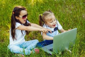 dos niños jugando ordenador portátil o cuaderno en el jardín para educación. linda muchachas acecho dibujos animados en ordenador personal pantalla.la concepto es inteligente aprendizaje desde Internet y social medios de comunicación foto