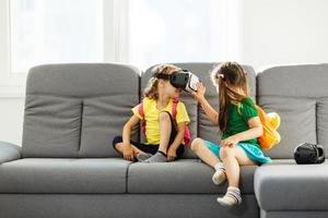 Lifestyle shot of an amazed two little kids using a virtual reality goggles with mouth open shocked seated in the living room at home. family activity concept. photo