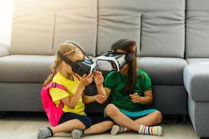 Lifestyle shot of an amazed two little kids using a virtual reality goggles with mouth open shocked seated in the living room at home. family activity concept. photo