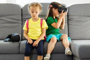 Lifestyle shot of an amazed two little kids using a virtual reality goggles with mouth open shocked seated in the living room at home photo