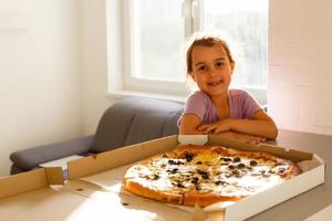 linda pequeño niña comiendo sabroso Pizza a hogar foto