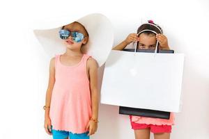 Cute fashion kids are standing together. Little girl in straw hat and striped red dress and little boy in white shirt in the studio on white background. Vacation, friendship, fashion for children photo