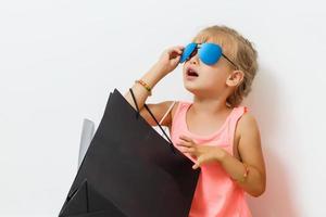 Pretty little blonde girl in a short holding shopping bags. The girl's parents go to the store to shop-Isolated on white background photo