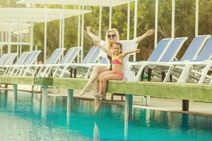 retrato de sonriente hermosa mujer y su pequeño linda hija en Gafas de sol cerca piscina al aire libre foto