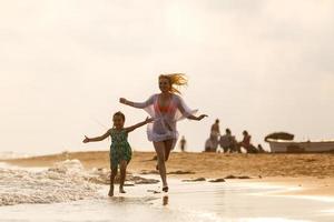 Happy family mother and child daughter run, laugh and play at beach photo