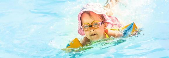 Happy little girl playing with colorful inflatable ring in outdoor swimming pool on hot summer day. Kids learn to swim. Child water toys. Children play in tropical resort. Family beach vacation. photo