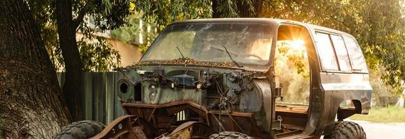 Close-up of an old rusty car with a broken door and no wheels on the background of a green coniferous forest photo