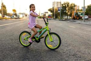 niños aprendizaje a conducir un bicicleta en un entrada de coches afuera. pequeño muchachas montando bicicletas en asfalto la carretera en el ciudad vistiendo cascos como protector engranaje. foto