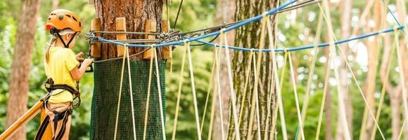 Portrait of cute little girl walk on a rope bridge in an adventure rope park. photo