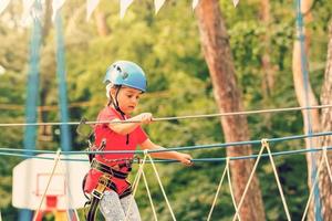 Portrait of cute little girl walk on a rope bridge in an adventure rope park. photo