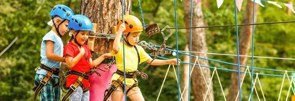 niño en bosque aventuras parque. niños escalada en alto cuerda camino. agilidad y alpinismo al aire libre diversión centrar para niños. pequeño niña jugando al aire libre. colegio yarda patio de recreo con cuerda forma. foto