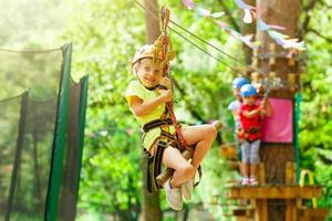 Brave young girl in helmet climbs on tree tops in amusement rope park on summer holidays, children camp photo