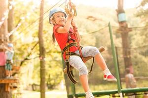 Brave young girl in helmet climbs on tree tops in amusement rope park on summer holidays, children camp photo