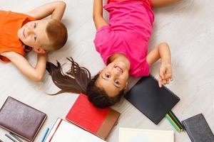 Kids drawing on floor on paper. Preschool boy and girl play on floor with educational toys - blocks, train, railroad, plane. Toys for preschool and kindergarten. Children at home or daycare. Top view photo