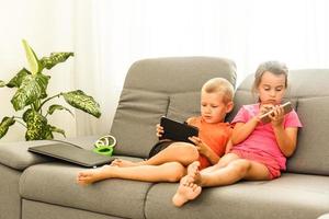 brother and sister sitting on couch at home using mobile phone. Close up surprised daughter and frustrated son looking at device screen. Technology new generation addicted with gadgets concept photo