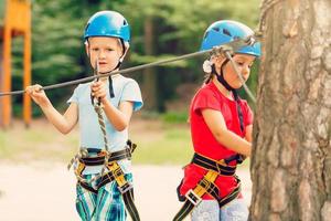 Children - a boy and a girl in the rope park pass obstacles. Brother and sister climb the rope road photo