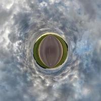 tiny planet in blue overcast evening sky with beautiful clouds with transformation of spherical panorama 360 degrees. Spherical abstract aerial view. Curvature of space. photo