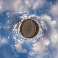 tiny planet in blue overcast evening sky with beautiful clouds with transformation of spherical panorama 360 degrees. Spherical abstract aerial view. Curvature of space. photo