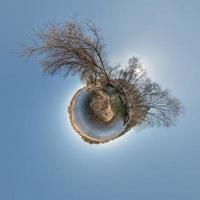 green tiny planet in blue sky with sun and beautiful clouds. Transformation of spherical panorama 360 degrees. Spherical abstract aerial view. Curvature of space. photo