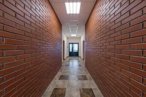 white empty long corridor with red brick walls and doors in interior of modern apartments or office photo