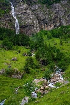 a waterfall that flows down a high cliff and flows into a stream photo