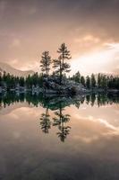 A lake in winter, on which stands a rock with two trees, during a sunset photo