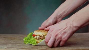 proche en haut de caucasien homme mains prendre une juteux Burger de une en bois tableau. homme choix en haut cheeseburger de table sur vert Contexte. video