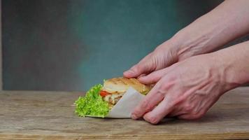 A Caucasian Man's Hands Take a juicy Burger from a wooden table. Man picks up Cheeseburger from table on green background. Close up video