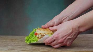un caucásico del hombre manos laico un apetito hamburguesa en un de madera mesa. hombre pone hamburguesa con queso en mesa en verde antecedentes. cerca arriba
