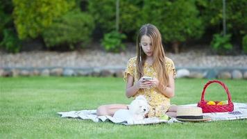 Jeune fille sur une couverture dans le herbe avec portable et panier de fruit video