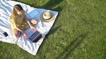 Young girl on a blanket in the grass with laptop and basket of fruit video