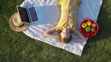 jung Mädchen auf ein Decke im das Gras mit Laptop und Korb von Obst