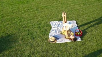 Jeune fille sur une couverture dans le herbe avec portable et panier de fruit video