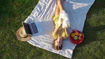 ung flicka på en filt i de gräs med bärbar dator och korg av frukt video