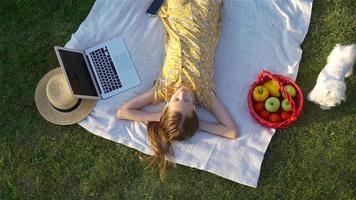 Jeune fille sur une couverture dans le herbe avec portable et panier de fruit video