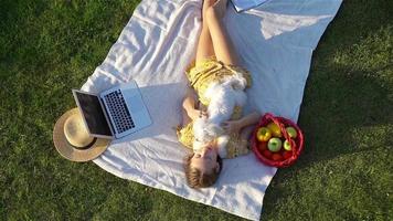 Young girl on a blanket in the grass with laptop and basket of fruit video