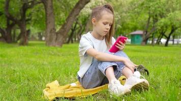 jong meisje zittend Aan gras met slim telefoon video