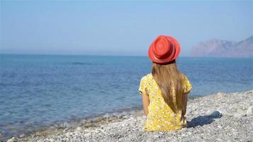 jong meisje zittend Aan strand vervelend roze hoed video