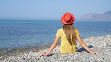 jovem menina sentado em de praia vestindo Rosa chapéu video