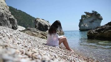 Adult woman sits on rocky beach side view video