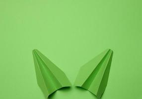 Green paper airplane on a green background, travel concept, top view. Copy space photo