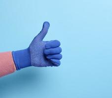 Female hand in blue work protective glove shows the gesture like on a blue background photo