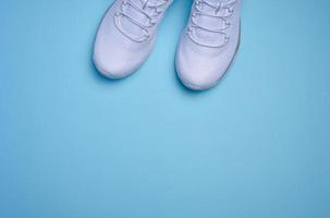 White textile sneakers on a blue background, top view photo