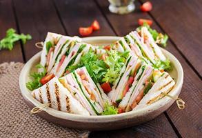 Club sandwich with ham, tomato, cucumber, cheese,  and arugula on wooden background. photo