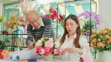 Aziatisch jong mooi vrouw bloemist arbeider en senior Mens winkel eigenaar regelen van bloesems boeket samen in valentijn, gelukkig werk met glimlach en vrolijk in kleurrijk bloem op te slaan, mkb ondernemer. video