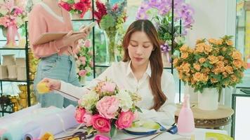 One young beautiful Asian female florist worker arranging and decorating bunch of fresh blossoms, valentine orders, smiling with happy work in colorful slower shop, small business SME entrepreneur. video