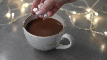 Marshmallows fallen lassen Tasse mit köstlich heiß Schokolade Kakao trinken. Beleuchtung sind auf im das Hintergrund. schleppend Bewegung