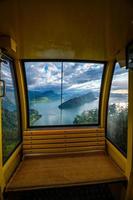 A cable car photographed from inside, from the window view you see a lake with mountains photo