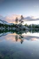 A lake in winter, on which stands a rock with two trees, during a sunset photo